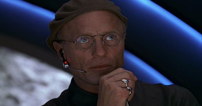 A man in a beanie and glasses listens intently through an earpiece with a worried, hand-on-chin expression, echoing the tension of the post about Bitcoin's volatility and the anxiety of those holding investments as prices approach $50k.