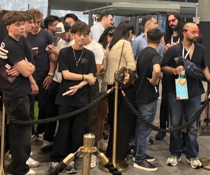 A group of young people, likely influencers, wait in line behind a velvet rope at a venue called Avenue, with one person holding a small shopping bag featuring colorful designs. The scene reflects the post's humorous observation about crypto influencers facing rejection or difficulty getting into the upscale venue, with the crowd appearing casual yet eager as they wait behind the rope barrier.