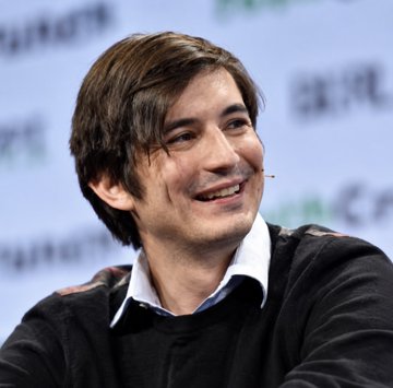 A smiling young man in a black sweater appears at a press conference or panel event, with partial Chinese text visible on the backdrop. The image of Vlad Tenev, co-founder and CEO of Robinhood, connects to the post announcing Robinhood's ($HOOD) bullish $25 million Bitcoin acquisition for its balance sheet.