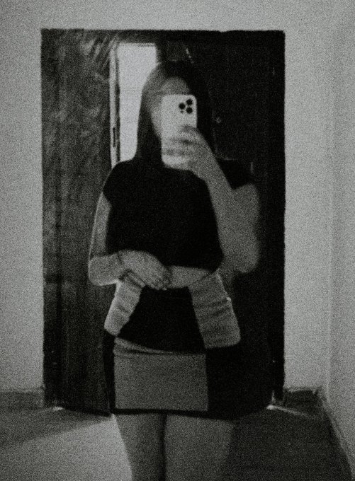 A grainy black-and-white mirror selfie shows a person in a dark top and skirt taking a photo with their phone, their face obscured by the device. The image accompanies a social media post promoting "$ansem" by "@blknoiz06" as part of a "day 3" campaign to reach 1 million holders, with the anonymous, phone-obscured aesthetic reinforcing the memecoin's community-driven branding.