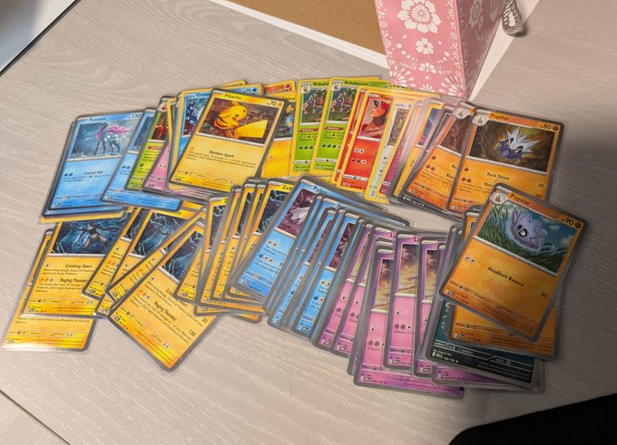 A collection of Pokémon trading cards, including Cosmos holos like Sandshrew, Ponyta, Doduo, and Seadra, spread out on a light wooden floor near a pink floral bag, illustrating the lucrative yet often underappreciated market for these holographic cards.