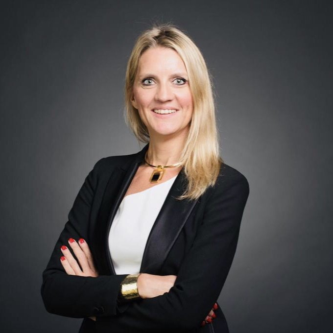A professional headshot of a smiling blonde woman with crossed arms, wearing a black blazer over a white top with a gold pendant necklace, against a gray background. The image accompanies a post announcing Aurélie Dhellemmes' promotion to Head of Global RWA at Digital Asset, highlighting her transition from her role as a long-time Ripple X VP to her new position at the Canton Network developer.