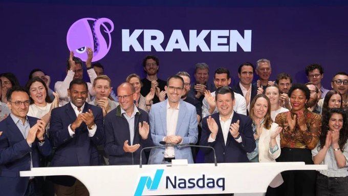 Kraken cryptocurrency exchange executives and employees celebrating at the Nasdaq stock exchange, with the Kraken logo displayed on a large purple screen behind them.