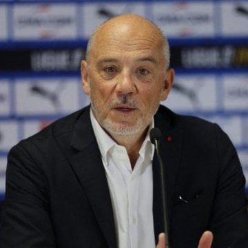 A bald man with a gray beard in a dark suit speaks at a press conference, with a backdrop featuring Puma and Ligue 1 logos. The image appears to accompany an announcement regarding Olympique de Marseille's new partnership with Chiliz Group, likely showing a club official discussing the blockchain collaboration.