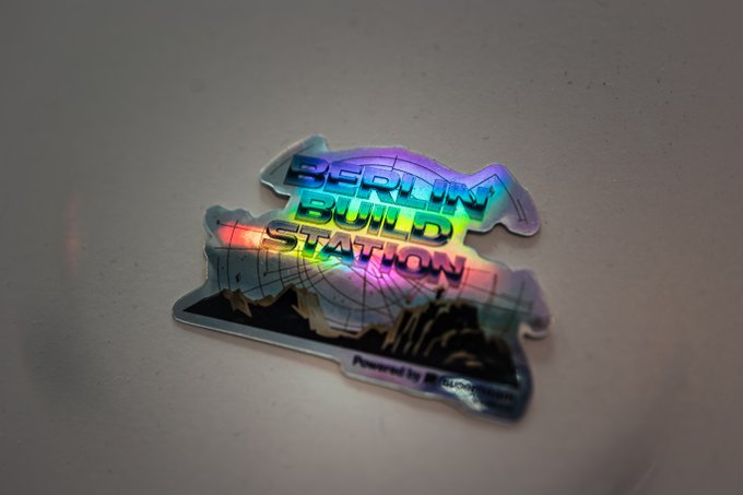 A holographic sticker labeled 'BERLIN BUILD SITATION' with city skyline imagery glows in rainbow colors on a surface.