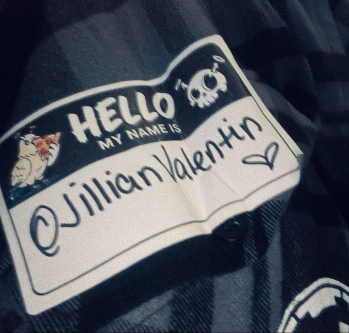 A 'Hello My Name Is' sticker on a plaid shirt with the name 'Jillian Valentin' written on it, featuring skull and rat graphics.