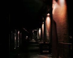 A very dark, low-light photograph of a nighttime city street showing building facades illuminated by faint, warm street lamps.
