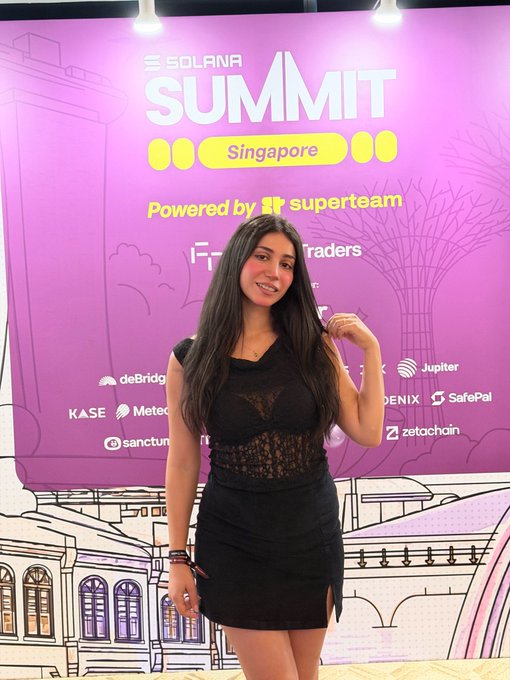 A young woman posing at the 'SOLANA SUMMIT Singapore' event backdrop, which features sponsor logos like Superteam, Jupiter, Phoenix, and SafePal.