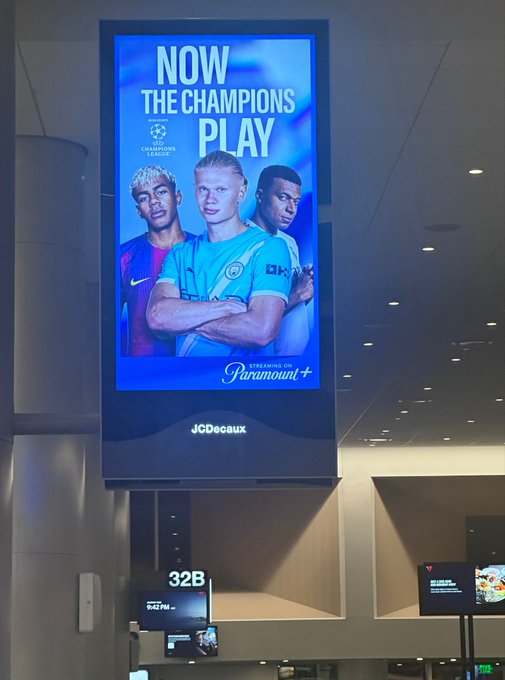A digital advertisement on a tall display reads 'NOW THE CHAMPIONS PLAY' featuring soccer players including Erling Haaland, with 'UEFA Champions League' and 'Streaming on Paramount+' logos visible, alongside 'JCDecaux' branding below.