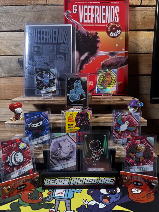 A display of Veefriends merchandise, including a comic book, trading cards, and figurines arranged on a wooden surface with a 'READY PLAYER ONE' sign at the bottom.