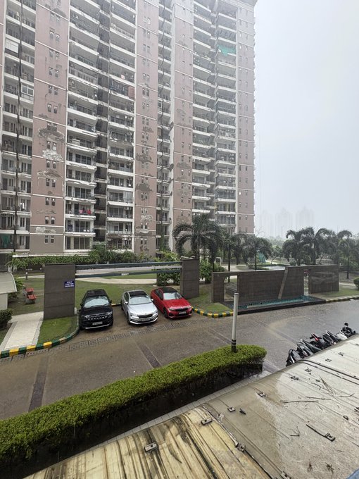 A view of high-rise residential apartment buildings overlooking a parking area with three cars and palm trees.