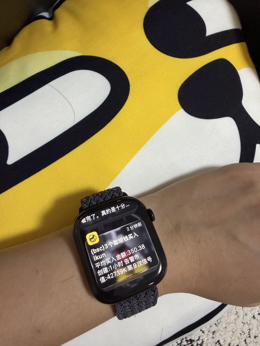 A wrist wearing an Apple Watch displays a 2-minute-old push notification from the channel "BSC" titled "[bsc] 3个币啦战友 ikun," reporting a coin call on $ikun with an entry around 0.350, hit a 1-hour gain of 350.3%, and a value of 42.71K at 9th place, illustrating the post's point about catching real-time meme coin signals on the wrist.