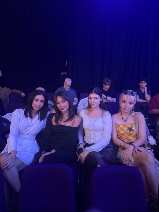 Four stylishly attired friends pose together in a dimly lit auditorium, with one wearing a star-patterned top and another holding a plush toy, perfectly capturing the glamorous "Crypto girl squad" vibe suggested by the post.
