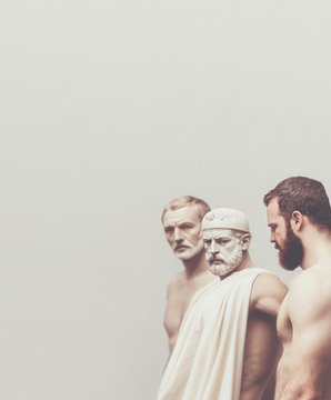 Three bearded men depicted in a classical or artistic style, with the central figure wearing a white toga and headband, flanked by two other men.