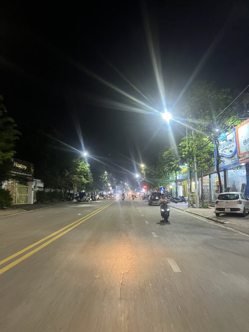 A nighttime street scene shows a motorcyclist riding down a well-lit road with bright streetlights and storefronts, including one labeled "Hana," on either side. The image of an open road under night lights pairs with the post's message about seizing opportunities, as the lone rider moving forward through the quiet street symbolizes perseverance despite missed chances.