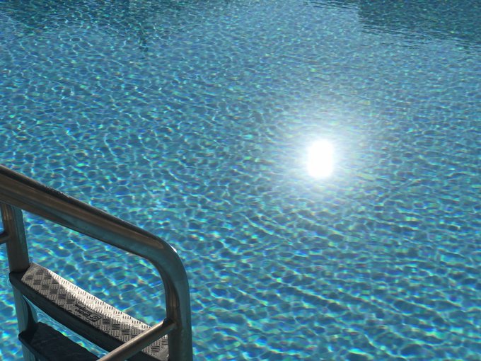 Crystal clear turquoise swimming pool water shimmering with sunlight reflections, featuring a metal handrail and tiled pool steps in the foreground.