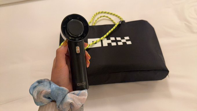A hand holds a black handheld cooling fan branded with the "OKX" logo, displayed alongside a matching black OKX-branded carrying pouch with a yellow-green lanyard. The image showcases the crypto exchange's practical merchandise giveaway, featuring their sleek branded fan designed for staying cool.