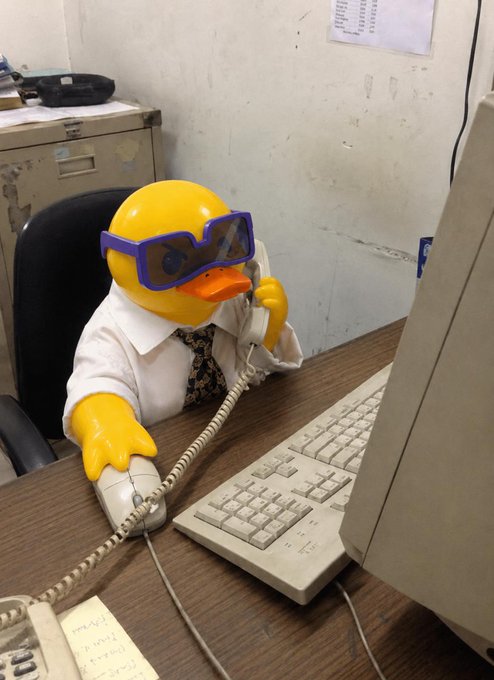 A humorous image of a rubber duck wearing glasses, a white shirt, and a tie, sitting at a desk and holding a telephone receiver.