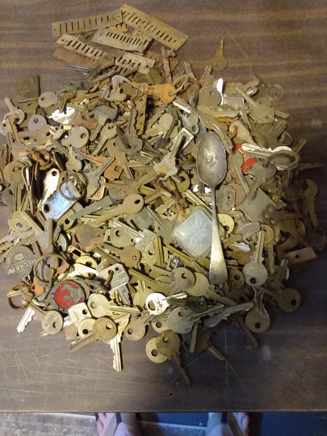A large pile of antique brass keys and a silver spoon scattered on a wooden surface.