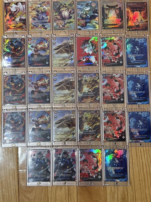 A collection of foil/holographic trading cards laid out on a wooden floor, featuring various character illustrations across multiple rows.