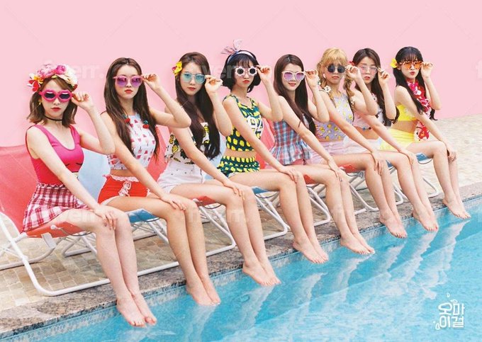 A K-pop promotional photo of nine female idols from Cosmic Girls (WJSN) sitting in a row on pool chairs, all wearing colorful summer outfits and sunglasses by a swimming pool with a pink backdrop.