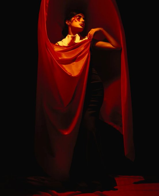 A dramatic photo shows a woman wearing red-tinted sunglasses and holding up a flowing red fabric against a dark background.