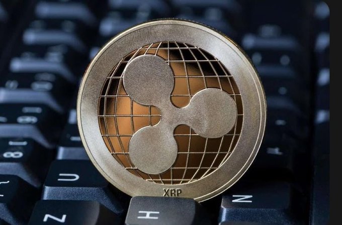 A close-up photo of a gold-colored XRP (Ripple) cryptocurrency coin resting on a black computer keyboard.