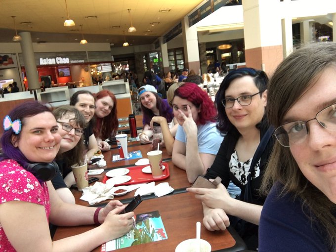 A casual selfie-style group photo of several women sitting around a table in a food court, with an 'Asian Chao' restaurant sign visible in the background.