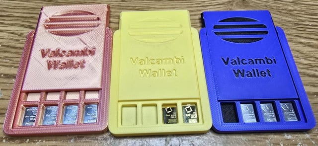 Three 3D-printed Valcambi Wallet coin/bullion holders in rose gold, gold, and blue colors, each containing small silver and gold bullion pieces in their slots.