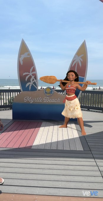 An AR figurine of Moana holding a paddle is displayed on the Myrtle Beach boardwalk, promoting the VeVe digital collectibles app.
