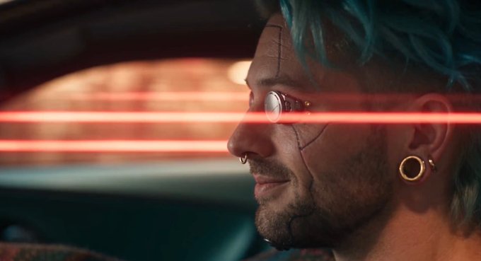 A close-up profile shot of a man with blue hair, facial scars, a nose ring, earring, and round glasses, with red light streaks across the frame, suggesting a cyberpunk aesthetic.