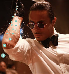 An image of a man wearing round sunglasses, a white shirt, and a black bowtie, reaching toward the camera with his hand.