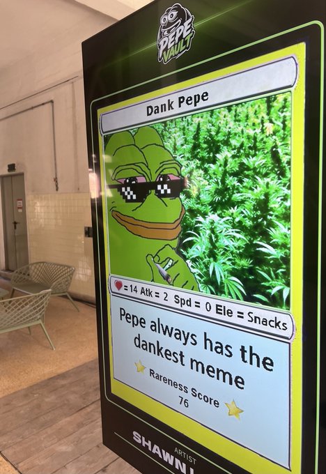 The image features a poster of a cartoon frog wearing sunglasses, which has been placed on display at an event or booth. The poster includes text that reads "DANKPEPE by @shawnleary S1 - C5 Rare Pepe". This suggests that the poster is promoting a product or service related to the character "Dank Pepe", possibly as part of a marketing campaign for a brand, product, or event.