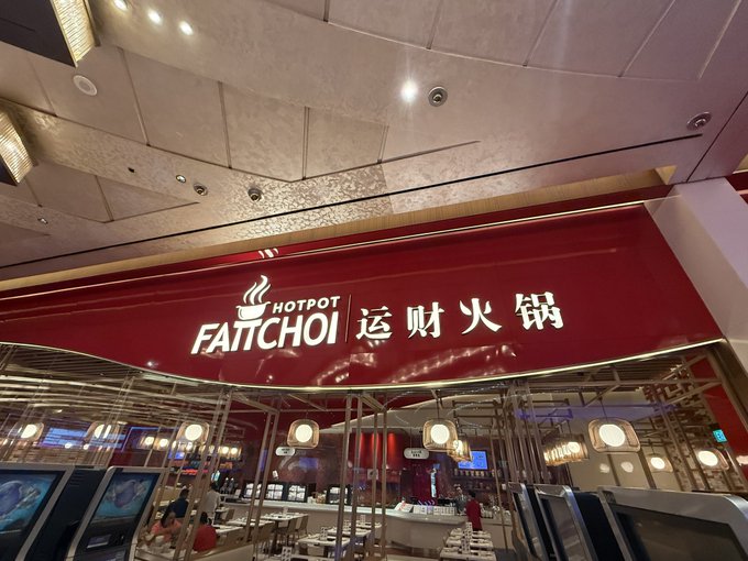 The illuminated red storefront sign for 'FAITCHOI HOTPOT 运财火锅' in a shopping mall.