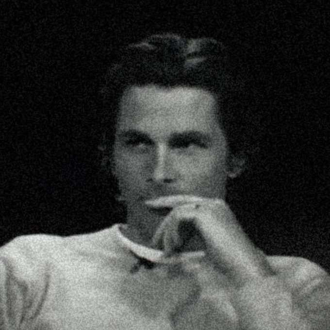 A grainy black and white portrait photograph of a young man with his hand near his face in a contemplative pose.