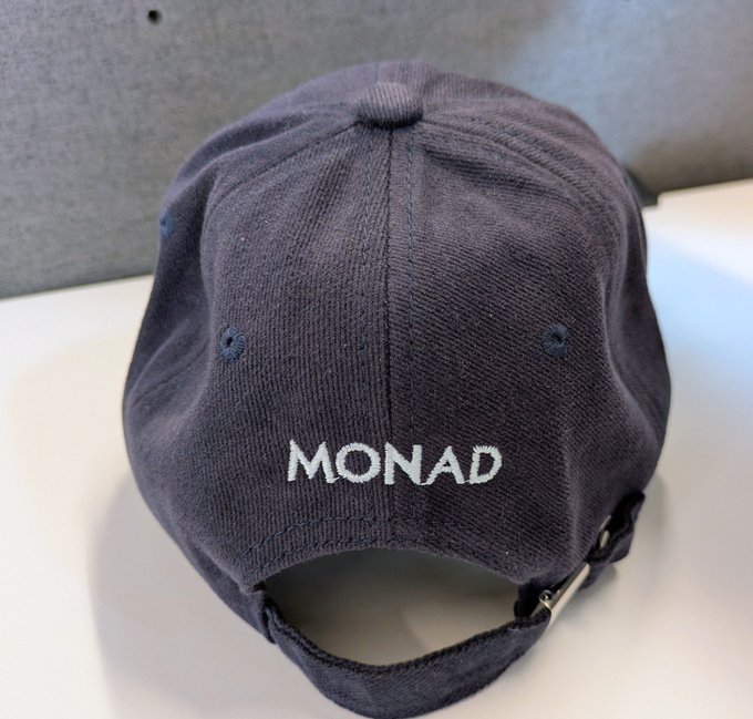 A navy blue baseball cap shown from the back with "MONAD" embroidered in white text above the adjustable strap.