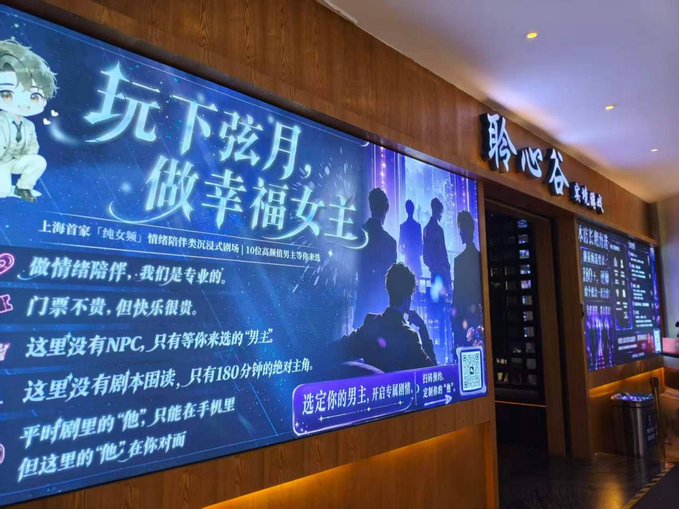 An illuminated advertisement in a Chinese shopping mall for a 'pure girl drama' experience, featuring an anime illustration and silhouettes of male characters under the heading '玩下弦月，做幸福女主'.