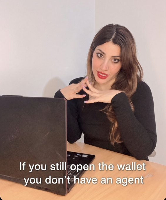 A woman with long brown hair and red lipstick sitting at a desk in front of a laptop, with overlay text reading 'If you still open the wallet you don't have an agent'.