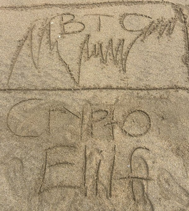 Words scratched into beach sand spell out "BITCOIN ON FIAT" across two panels, with a horizontal line dividing the message, reflecting the post's playful nod to Bitcoin advocacy even during a vacation.