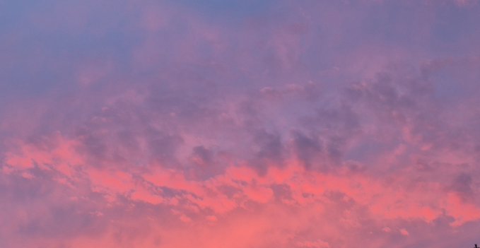 A serene photograph of a twilight sky filled with textured clouds tinted in soft shades of pink, purple, and blue.