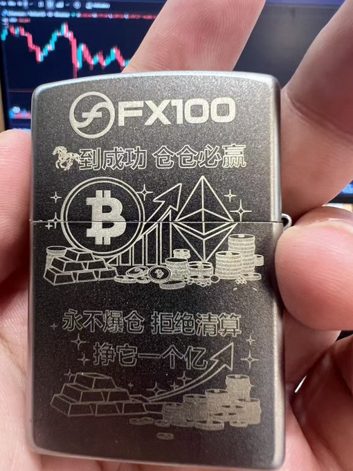 A close-up of a hand holding a metal Zippo-style lighter engraved with 'FX100', Bitcoin and Ethereum symbols, gold bars, and Chinese text including '挣到一个亿', with a trading chart visible on a monitor in the background.