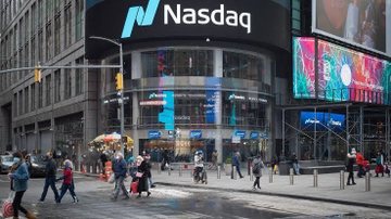 The Nasdaq stock exchange building and signage are visible on a busy city street corner in New York, with pedestrians crossing the intersection below.