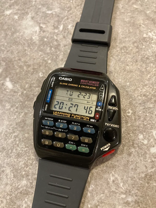 A vintage Casio digital wristwatch featuring a calculator and learning functions rests on a textured surface, displaying the time 20:27.