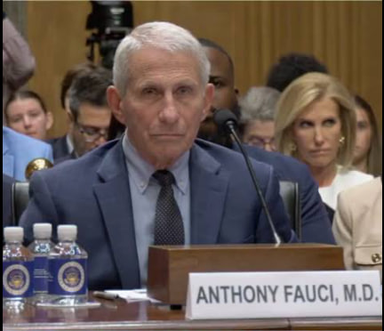 Anthony Fauci, M.D. seated at a congressional hearing table with a name placard and water bottles in front of him.