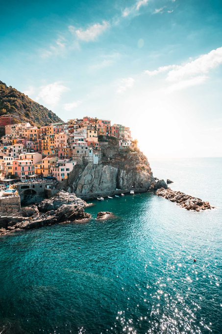 A scenic view of a colorful coastal town with pastel-colored buildings built on a rocky cliff overlooking bright blue ocean water.