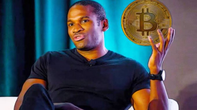 A man in a dark t-shirt holds up a large golden Bitcoin coin while seated on stage, with the image overlaid on a breaking news post about Arthur Hayes and BitMEX ceasing operations. The Bitcoin symbol visually reinforces the cryptocurrency exchange context of the announcement.