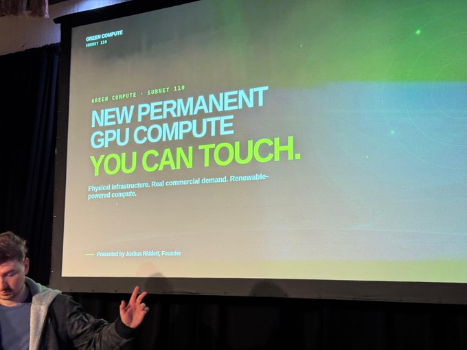 A man stands gesturing in front of a projected presentation slide titled "NEW PERMANENT GPU COMPUTE YOU CAN TOUCH" for Green Compute Subnet 110, presented by Joshua Riddett, Founder. The slide's messaging about permanent, renewable-powered physical GPU infrastructure directly complements the post's praise of Green Compute's approach to building compute facilities around existing underused renewable power rather than temporary setups.