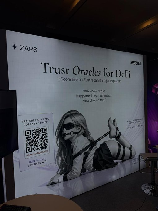 An indoor photo of a ZAPS/ZERUM promotional banner titled 'Trust Oracles for DeFi' with text 'zScore live on Etherscan & major explorers' and 'We know what happened last summer… you should too,' alongside a QR code and an illustration of a woman in bondage-style attire.