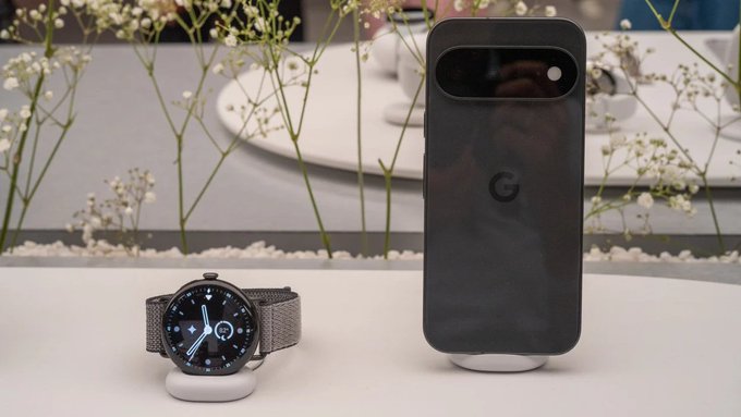 A Google Pixel smartphone and Pixel Watch are displayed on a table with white flowers in the background.