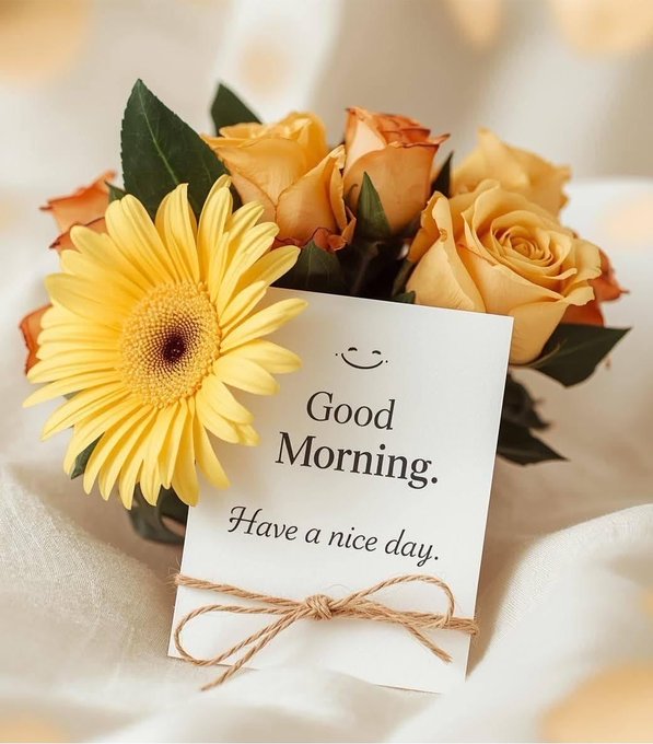 A greeting card reading 'Good Morning. Have a nice day.' is tied with twine, nestled among yellow gerbera daisies and peach-colored roses.
